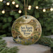 A round ornament with a painting of a scenic landscape, featuring a waterfall, desert, and a small house, hangs in front of a blurred background with twinkling lights.