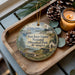 A decorative ornament featuring a scenic image of San Juan Island National Historical Park in Washington, with pine cones and a lit candle on a wooden tray.