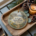 A wooden tray with a decorative ornament featuring a scenic landscape of Schafer State Park in Washington, accompanied by pine cones and a lit candle.