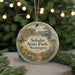 A round ornament with a scenic image of a park, featuring a mountain, lake, and pine trees, is hanging from a string.