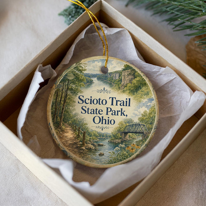 A decorative ornament in a box, featuring a scenic image of a trail and a bridge, with the text "Scio Trail State Park, Ohio" printed on it.
