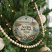 A round ornament hanging on a Christmas tree, featuring a lighthouse and a beach scene with birds and flowers.