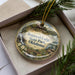 A decorative ornament in a box, featuring a scenic image of Sequoyah Lodge in Oklahoma State Park, with greenery and a natural landscape surrounding it.