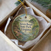 A decorative ornament in a white box, featuring a scenic landscape with a river, trees, and a bird.