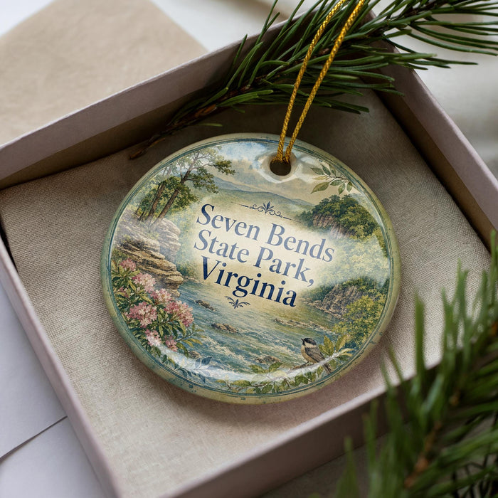 A decorative ornament in a box, featuring a scenic landscape with a river, mountains, and pine trees.