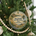 A round ornament hanging on a Christmas tree, featuring a scenic landscape with a river, mountains, and wildlife.