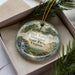A decorative ornament in a box, featuring a scenic landscape with a tower and greenery, with the text "Shot Tower Historical State Park, Virginia" printed on it.