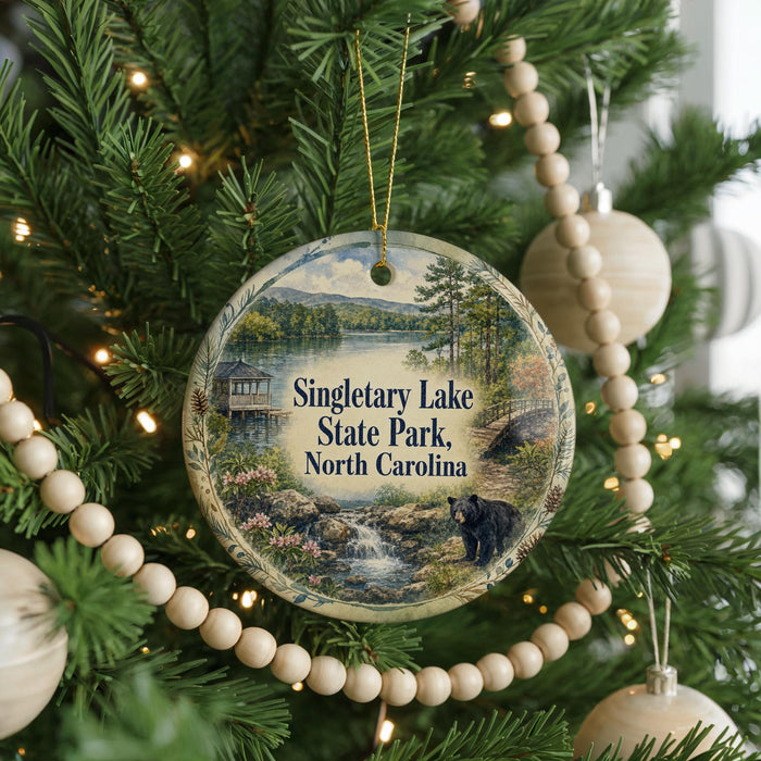 A round ornament hanging on a Christmas tree, featuring a scenic image of Singletary Lake State Park in North Carolina.