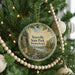 A round ornament hanging on a Christmas tree, featuring a scenic landscape with a river and mountains.