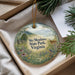 A decorative ornament with a nature scene, featuring a deer, flowers, and a bird, is displayed in a box with pine branches.