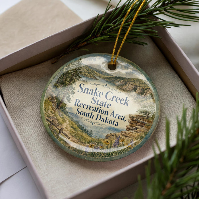A decorative ornament with a scenic landscape of Snake Creek State Recreation Area in South Dakota, featuring a mountain, river, and forest.