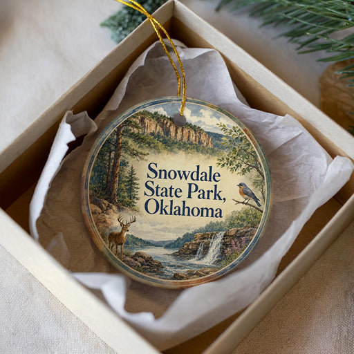 A decorative ornament in a box, featuring a scenic landscape with a waterfall, a bird, and a deer.