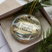A decorative ornament in a box, featuring a scenic landscape with a waterfall, trees, and wildlife.