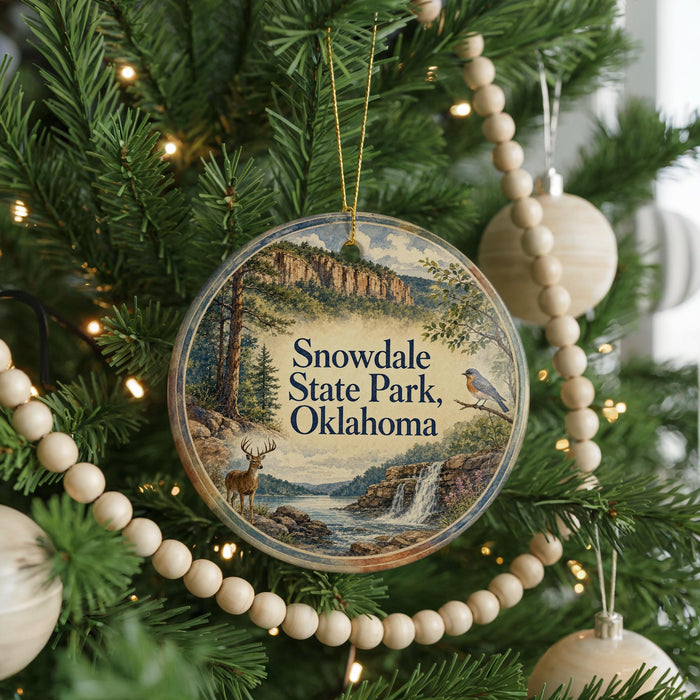 A circular ornament hanging on a Christmas tree, featuring a scenic landscape with a waterfall and a bird perched on a branch.