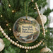 A circular ornament hanging on a Christmas tree, featuring a scenic landscape with a waterfall and a bird perched on a branch.