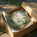 A round ornament in a box, featuring a lighthouse and a scenic landscape, with the text "South Bass Island State Park, Ohio" printed on it.