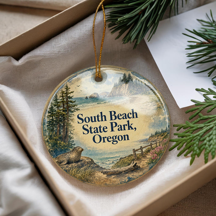A decorative ornament with a scenic landscape of South Beach State Park, Oregon, featuring pine trees, a body of water, and a rocky shoreline.