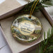 A decorative ornament in a box, featuring a scenic landscape with a waterfall, trees, and a bridge.