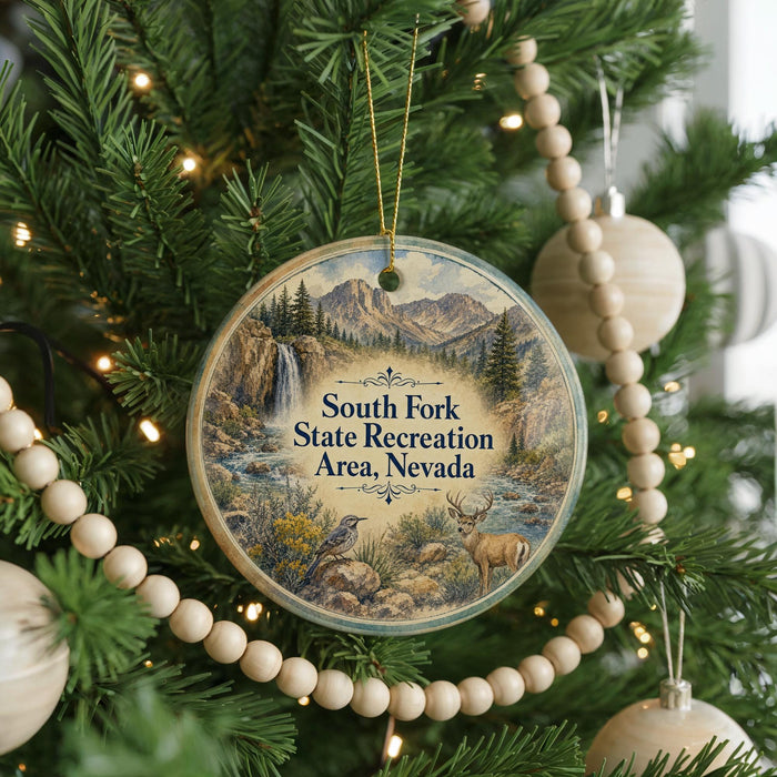 A round ornament hanging on a Christmas tree, featuring a scenic landscape with mountains, a waterfall, and a bird.