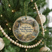 A round ornament hanging on a Christmas tree, featuring a scenic landscape with mountains, a waterfall, and a bird.