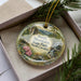 A decorative ornament in a box, featuring a scenic landscape with mountains, trees, and a bird, along with the text "South Mountains State Park, North Carolina".