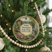 A round ornament hanging on a Christmas tree, featuring a scenic landscape with mountains, a waterfall, and a bird.