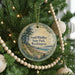 A round ornament hanging on a Christmas tree, featuring a scenic landscape with a beach and mountains.