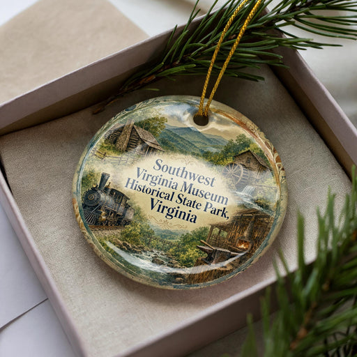 A decorative ornament in a box, featuring a scenic landscape with a train, buildings, and greenery.