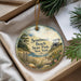 A decorative ornament with a beach scene and text, placed in a box with pine branches.