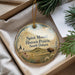 A decorative ornament with a picture of a bison in a field, surrounded by flowers and trees, placed in a box with pine branches.