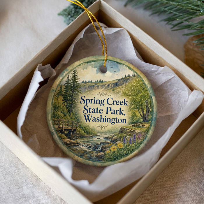 A decorative ornament in a box, featuring a scenic landscape with a river, trees, and mountains.
