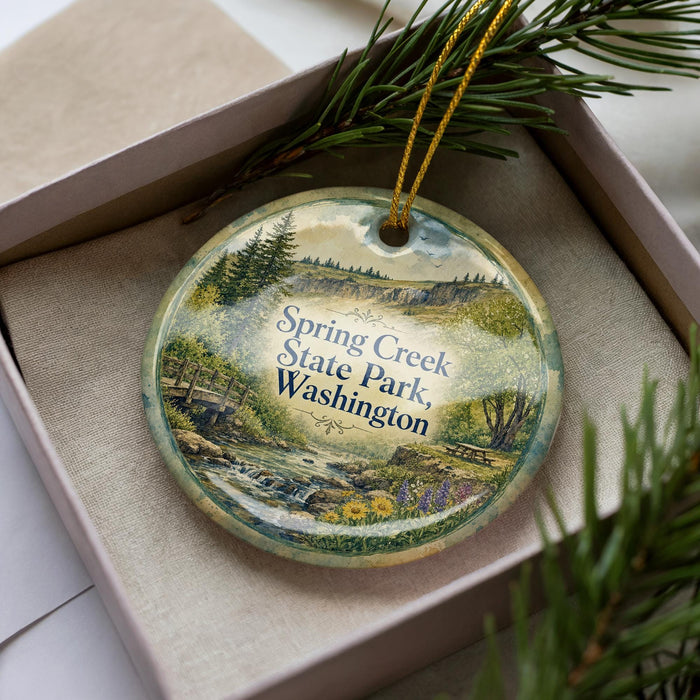 A decorative ornament with a scenic landscape of Spring Creek State Park in Washington, featuring a river, pine trees, and a bridge.