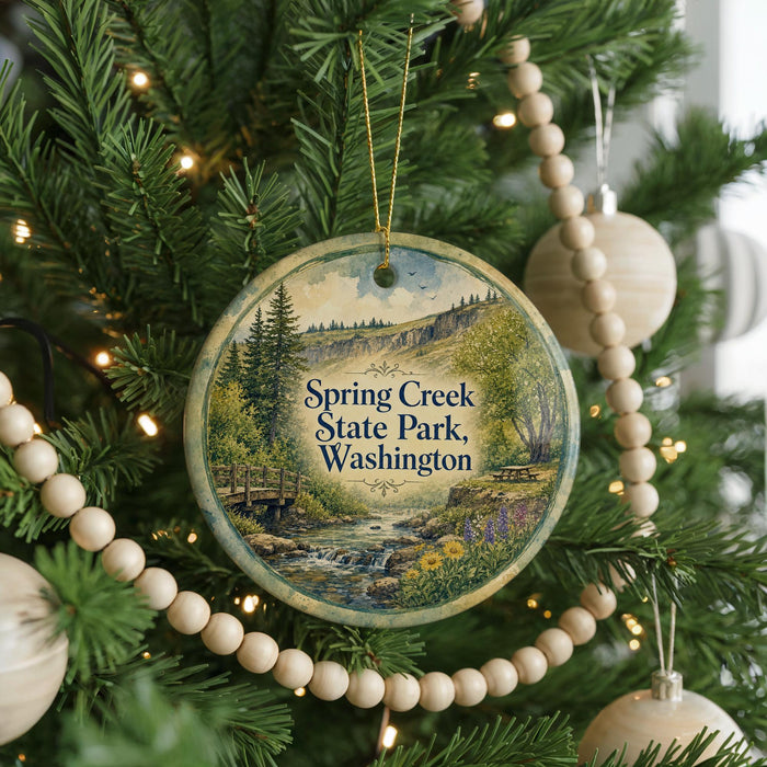 A round ornament hanging on a Christmas tree, featuring a scenic image of Spring Creek State Park in Washington.