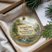 A decorative ornament with a scenic landscape of a river, mountains, and pine trees, hanging from a string.
