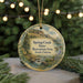 A round ornament with a scenic landscape of a mountain, river, and pine trees, hanging from a string.