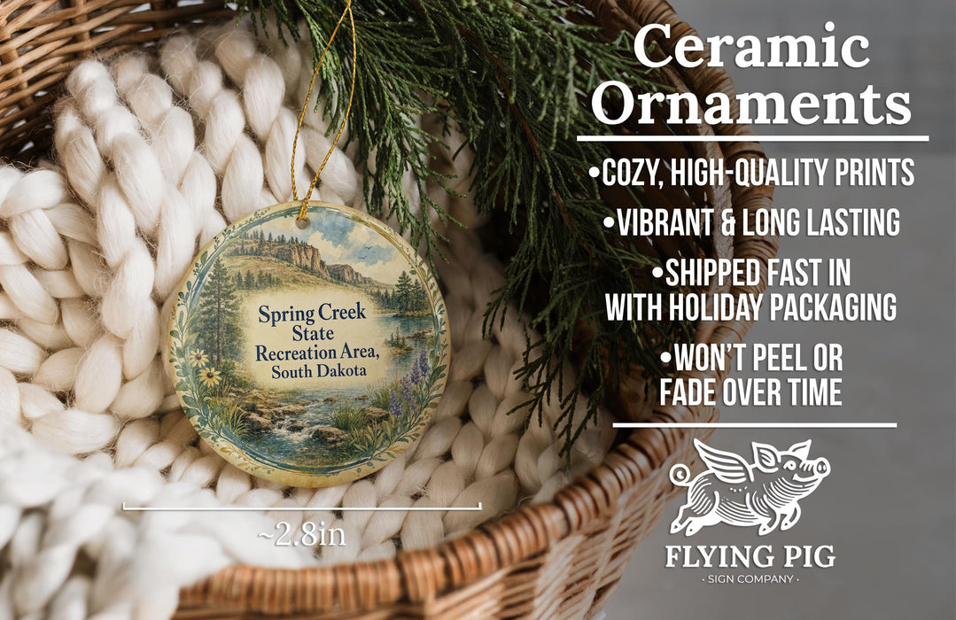 Ceramic ornaments, featuring a Spring Creek State Recreation Area ornament, are displayed in a basket with pine branches. The ornament is described as having a cozy, high-quality print, vibrant and long-lasting, and being shipped fast in holiday packaging. The ornament is not described as being peel-able or fade-resistant.