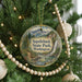 A circular ornament hanging on a Christmas tree, featuring a scenic landscape with mountains, a waterfall, and pine trees.