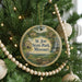 A round ornament hanging on a Christmas tree, featuring a scenic landscape with a waterfall and a house.