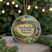 A round ornament with a scenic landscape featuring a waterfall and a bridge, surrounded by greenery and placed on a surface with a blurred background of lights.