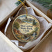 A decorative ornament in a box, featuring a scenic landscape with mountains, trees, and a waterfall.