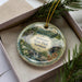 A decorative ornament with a scenic landscape of Stilwater State Park in Vermont, featuring a waterfall, pine trees, and a bridge.