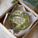A round ornament with a scenic landscape of Stonelick State Park, Ohio, displayed in a box with a white tissue paper lining.