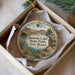 A decorative ornament in a box, featuring a scenic landscape with mountains, a lake, and a bird.