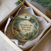 A decorative ornament in a white box, featuring a scenic image of a lake and surrounding nature.