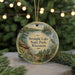 A round ornament with a scenic lake and forest landscape, featuring a boat and a bird, is displayed in front of a blurred background with twinkling lights.