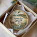 A decorative ornament in a box, featuring a scenic landscape with a lake, mountains, and a cabin.