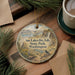 A decorative ornament featuring a scenic landscape with a waterfall, surrounded by pine branches and a bird perched on a rock.