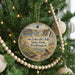A circular ornament hanging on a Christmas tree, featuring a scenic landscape with a waterfall and a bird perched on a rock.