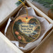 A decorative ornament in a box, featuring a scenic landscape with a sunset over a body of water and a path leading to a cliff.