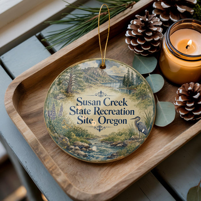 A wooden tray with a decorative ornament featuring a scenic landscape and a bird, along with pine cones and a lit candle, creating a cozy and rustic atmosphere.